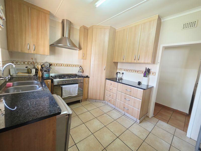 A functional kitchen featuring light wood cabinetry, granite countertops, a stainless steel gas stove with extractor fan, and tiled flooring.