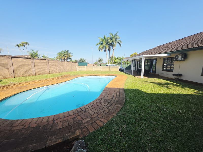 Spacious backyard featuring a swimming pool with brick coping, a well-maintained lawn, and a covered patio area attached to the main house.