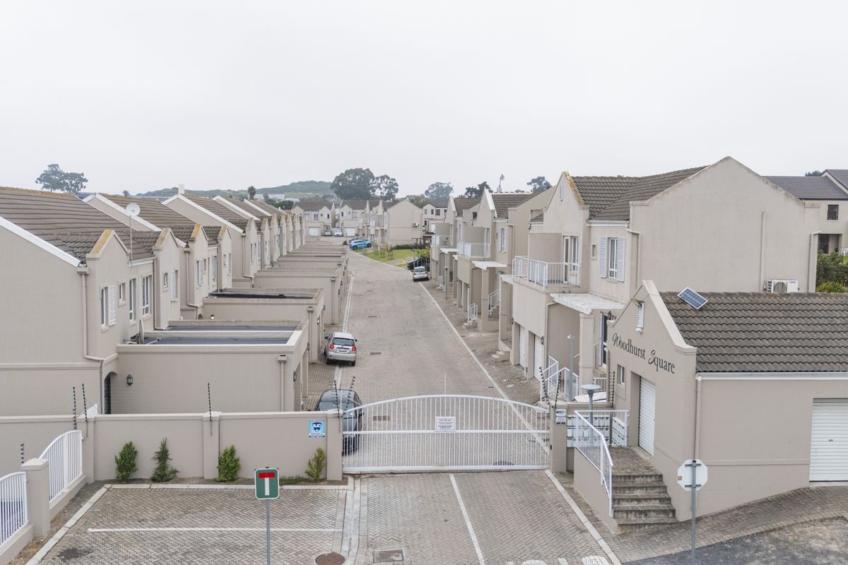 Aerial view of a townhouse complex entrance featuring paved driveways, security gates, and uniform residential units with tiled roofs.