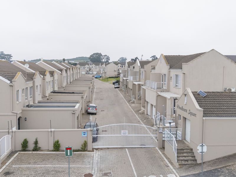 Aerial view of a townhouse complex entrance featuring paved driveways, security gates, and uniform residential units with tiled roofs.