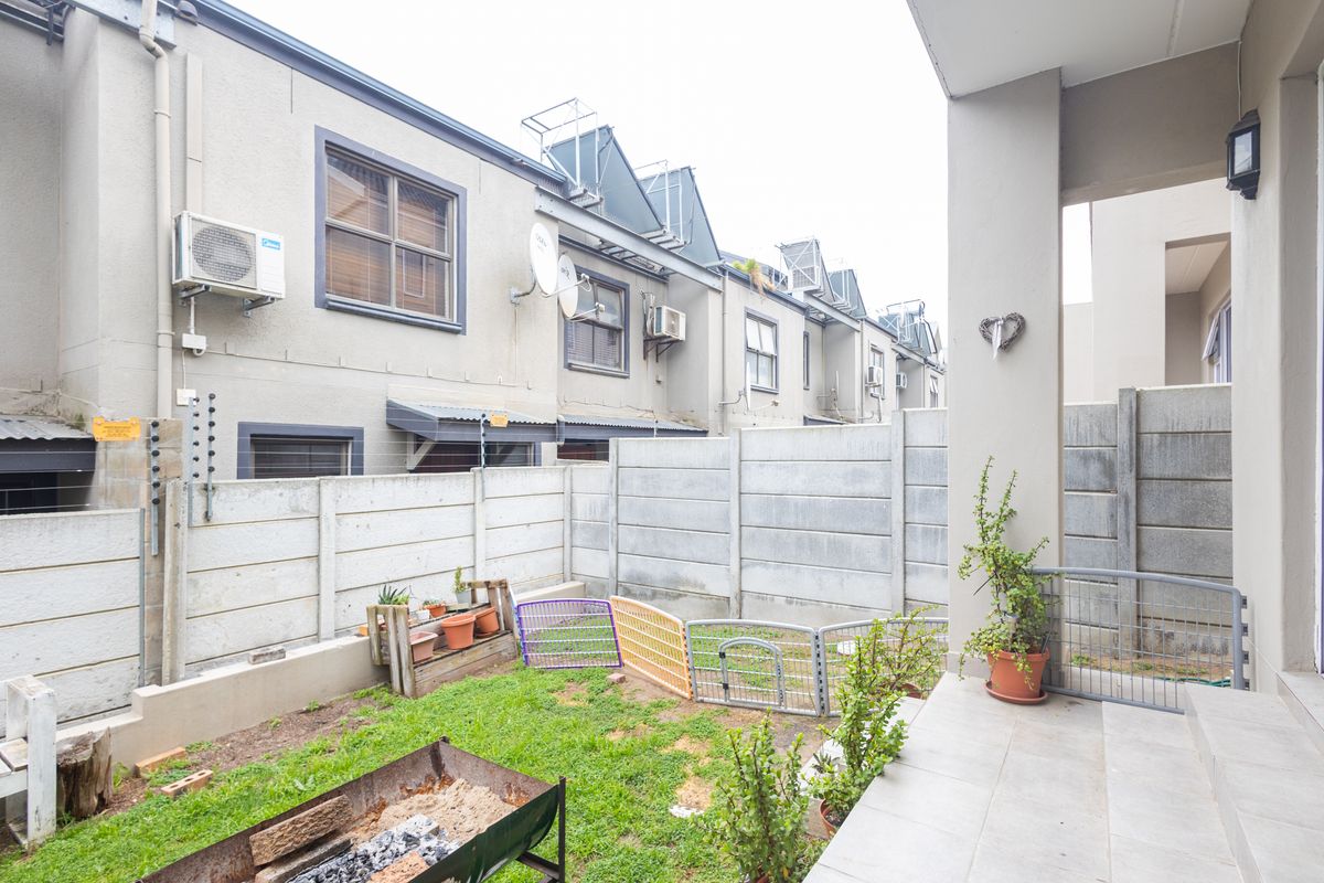 A private rear courtyard featuring a tiled patio area and a small garden enclosed by precast concrete walls with electric fencing.