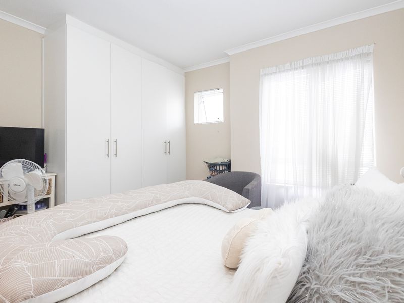 A bright bedroom featuring neutral walls, white built-in cupboards, and a window with sheer curtains, providing a clean and functional living space.