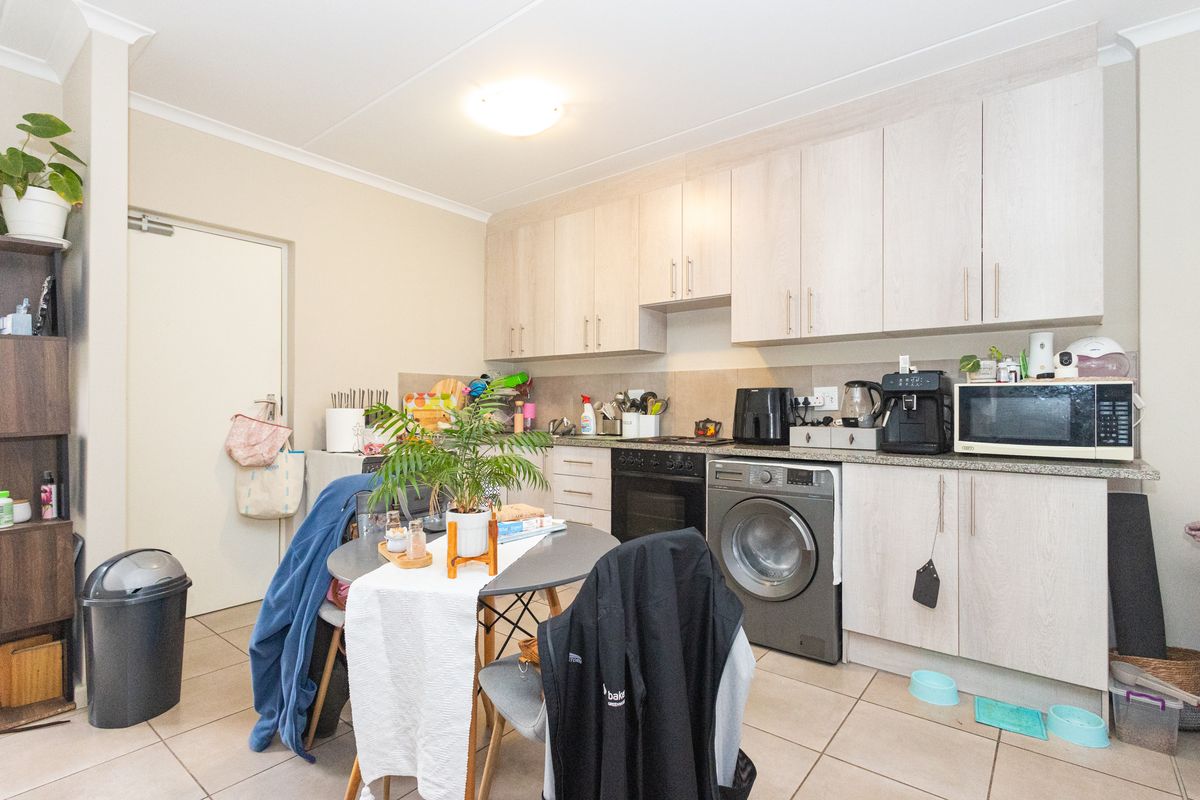 A functional kitchen featuring light wood-finish cabinetry, integrated appliances including a washing machine and oven, and neutral tiled flooring.