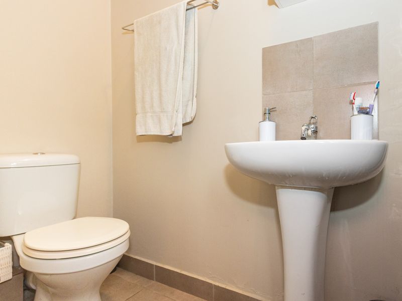 A functional bathroom featuring a white pedestal basin with a tiled splashback and a standard toilet.
