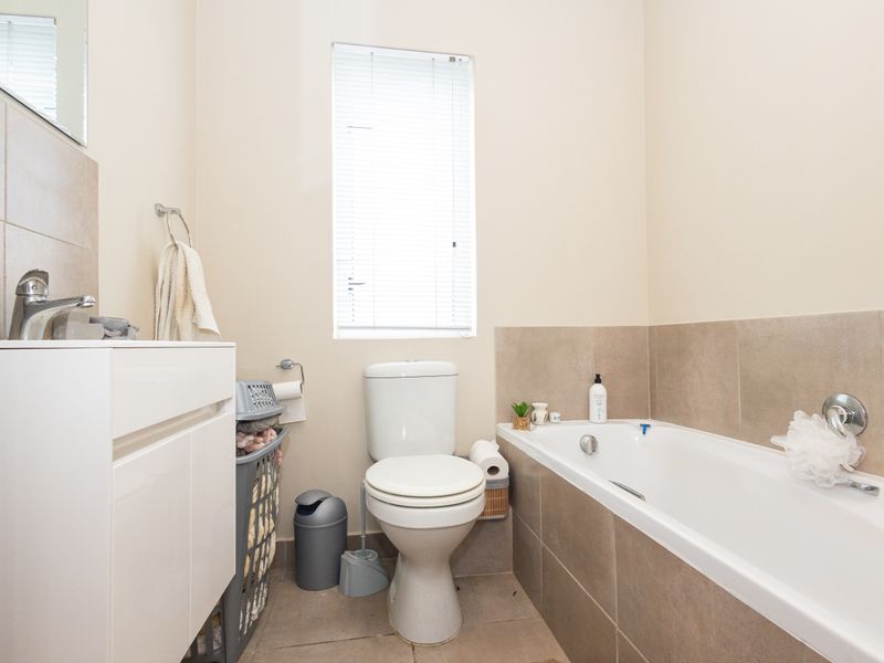 A functional bathroom featuring a white vanity, toilet, and a bathtub with neutral wall tiling and a window with a venetian blind.