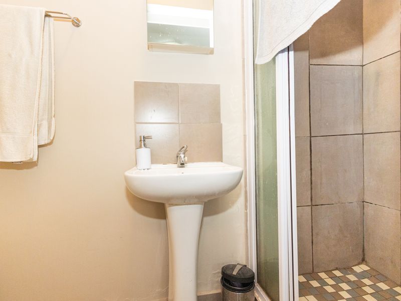 A functional bathroom featuring a pedestal basin, wall mirror, and a tiled shower enclosure with a glass door.