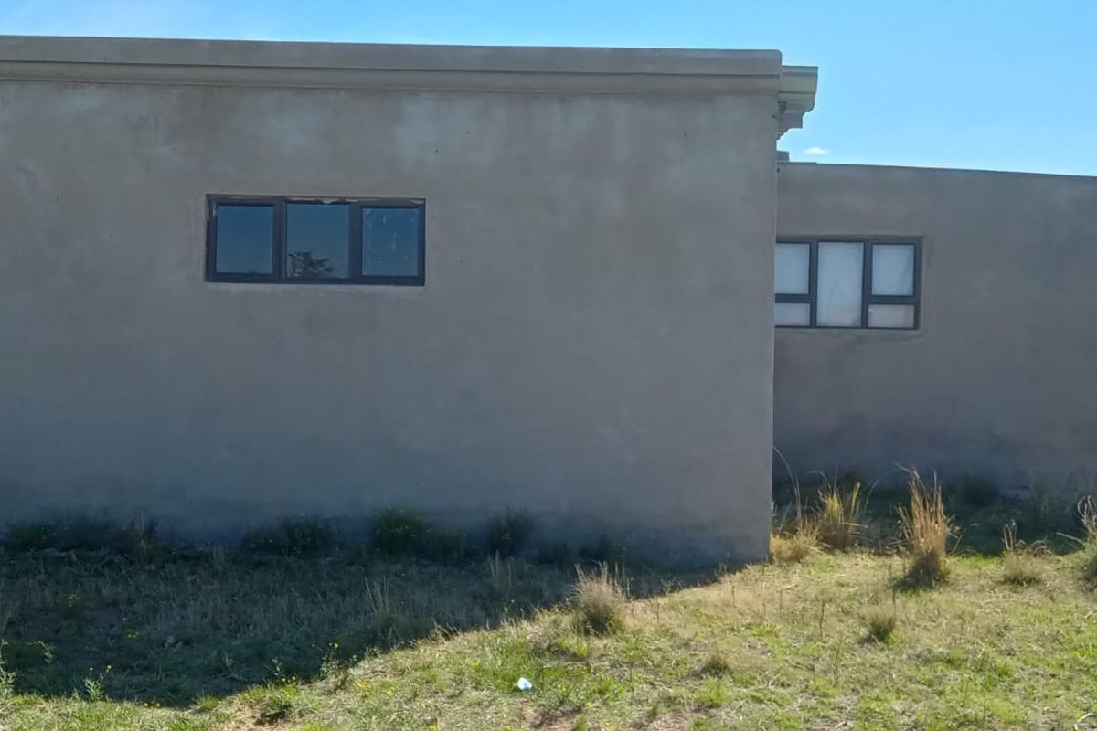 Rear view of a single-story house featuring unpainted cement plaster walls, aluminium window frames, and concrete support columns.