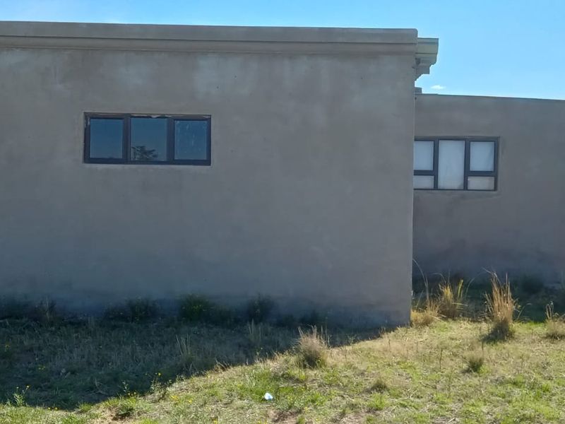 Rear view of a single-story house featuring unpainted cement plaster walls, aluminium window frames, and concrete support columns.