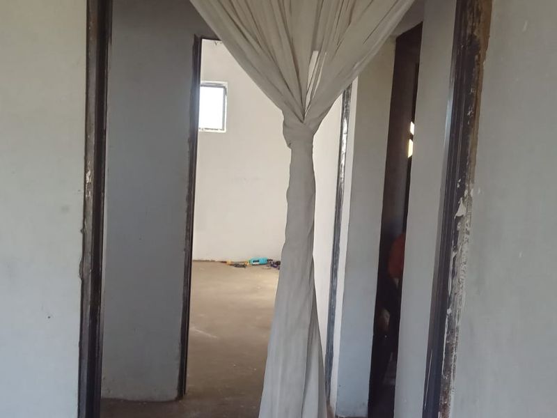 A view through a hallway showing unfinished interior walls and worn door frames in a property requiring renovation.