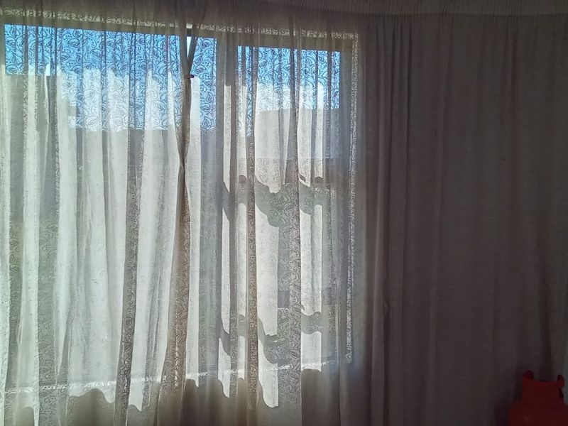 A sparsely furnished bedroom featuring a large window with curtains, providing natural light and a view of the exterior.