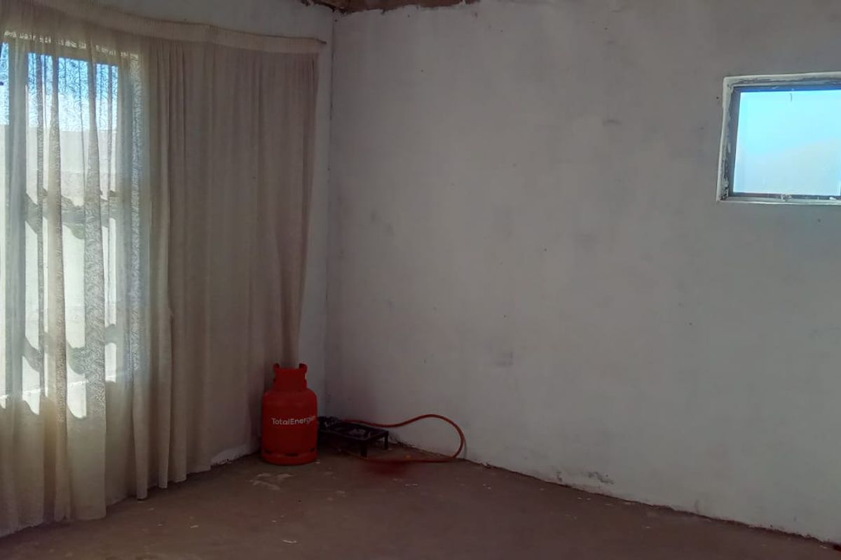 An empty living room space featuring large windows and unfinished wall and floor surfaces, offering a blank canvas for renovation.