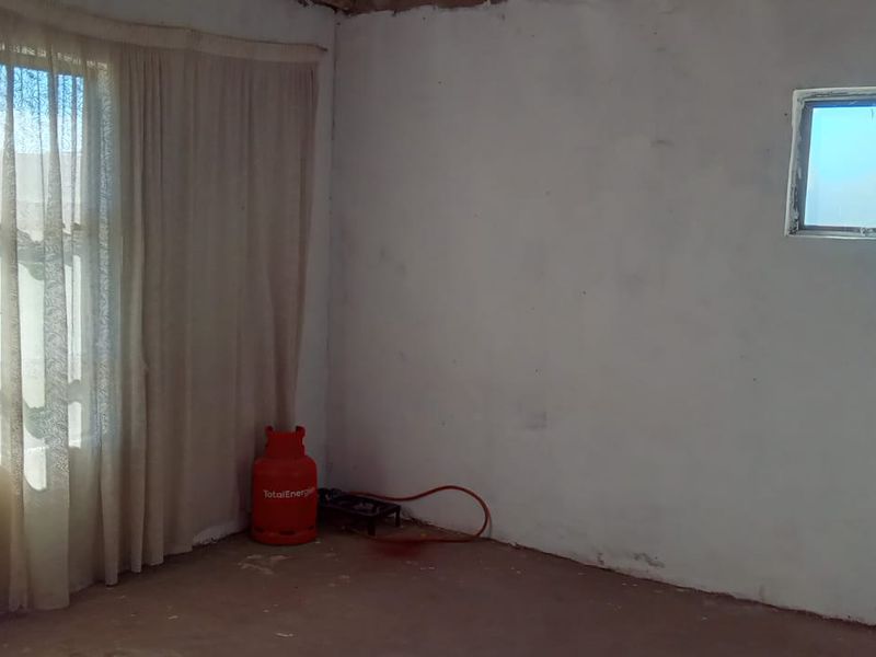 An empty living room space featuring large windows and unfinished wall and floor surfaces, offering a blank canvas for renovation.