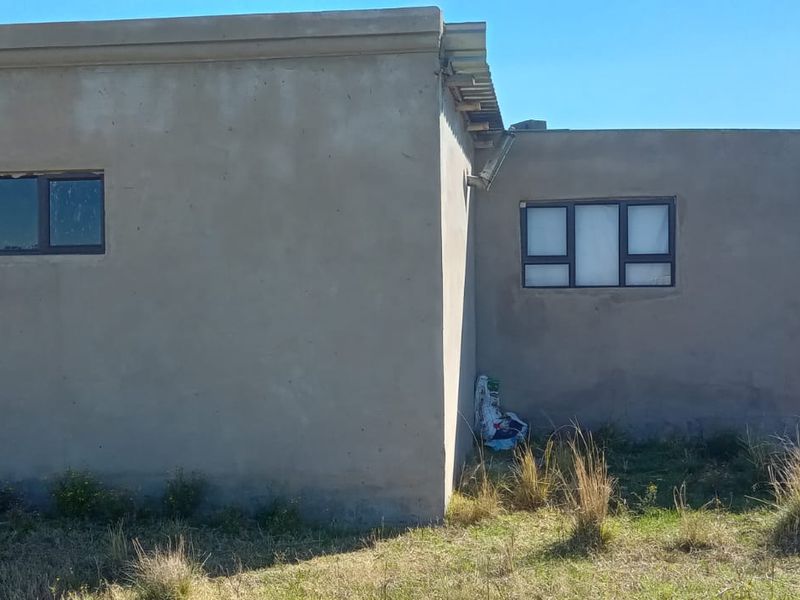Rear exterior view of the property featuring unpainted cement plaster walls, aluminium window frames, and a covered patio area with a concrete column.