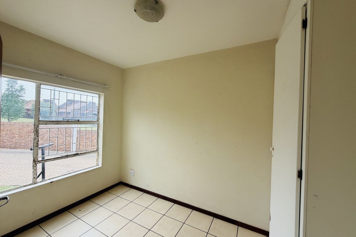 An empty bedroom featuring tiled flooring, a built-in cupboard, and a window fitted with security bars.