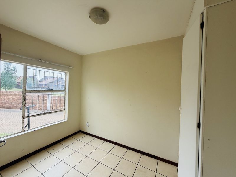 An empty bedroom featuring tiled flooring, a built-in cupboard, and a window fitted with security bars.