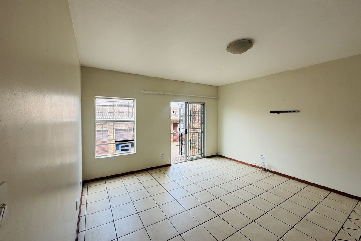 An empty living room featuring tiled flooring, a sliding glass door leading to an outdoor area, and security bars on the windows.
