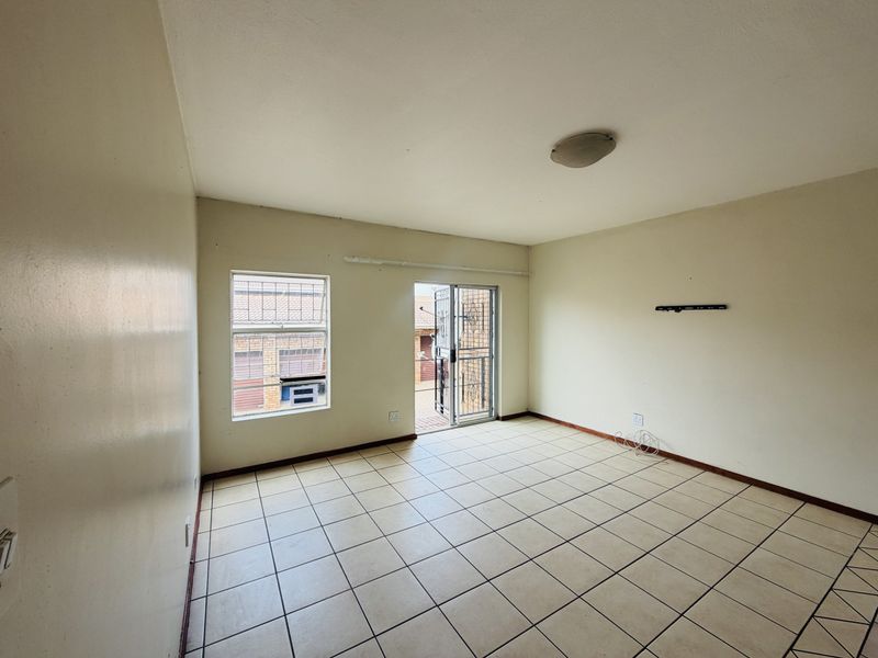 An empty living room featuring tiled flooring, a sliding glass door leading to an outdoor area, and security bars on the windows.
