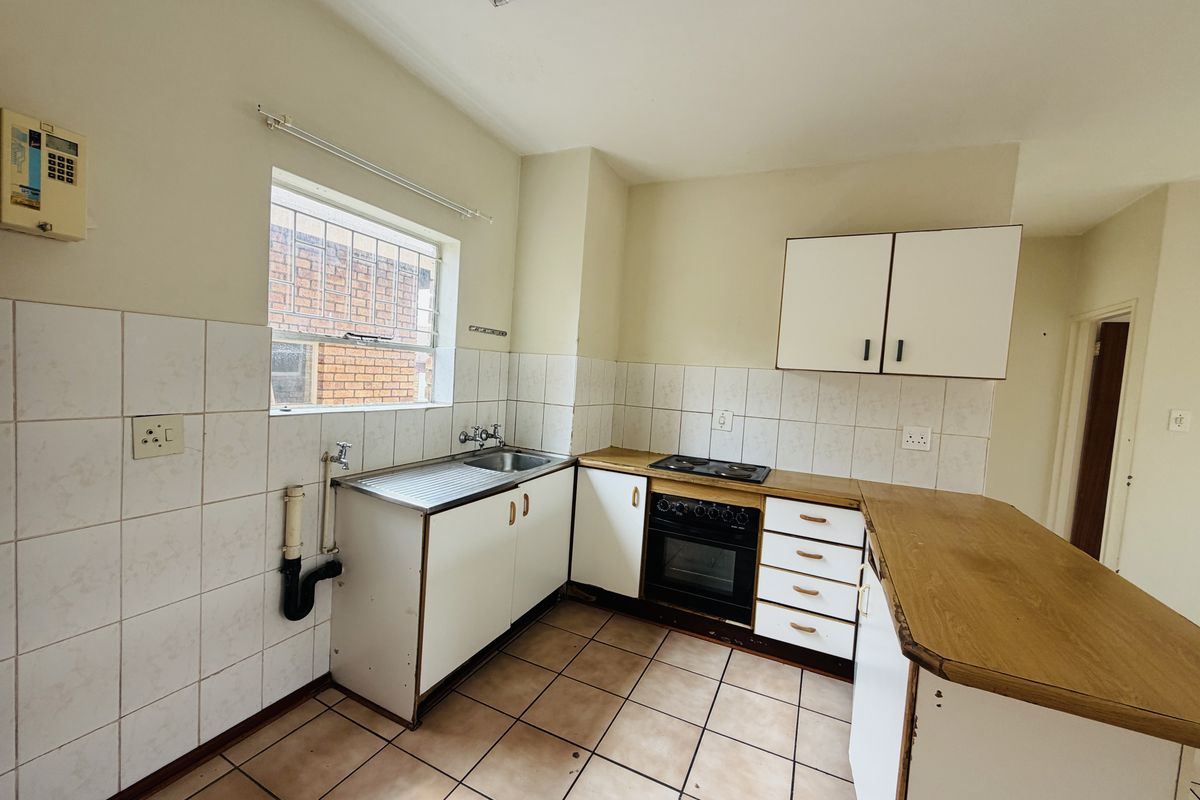 A functional kitchen featuring built-in cabinetry, a stainless steel sink, an electric hob, and an oven, with tiled flooring and splashbacks throughout.