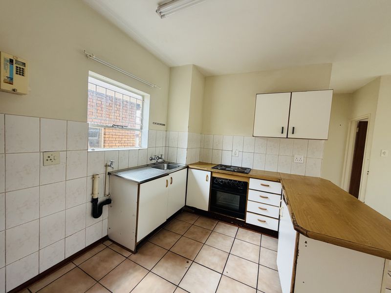 A functional kitchen featuring built-in cabinetry, a stainless steel sink, an electric hob, and an oven, with tiled flooring and splashbacks throughout.