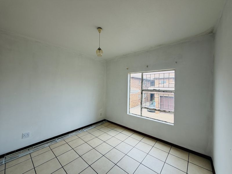 An empty bedroom featuring tiled flooring, a window with security bars, and a simple pendant light fitting, ready for renovation or staging.