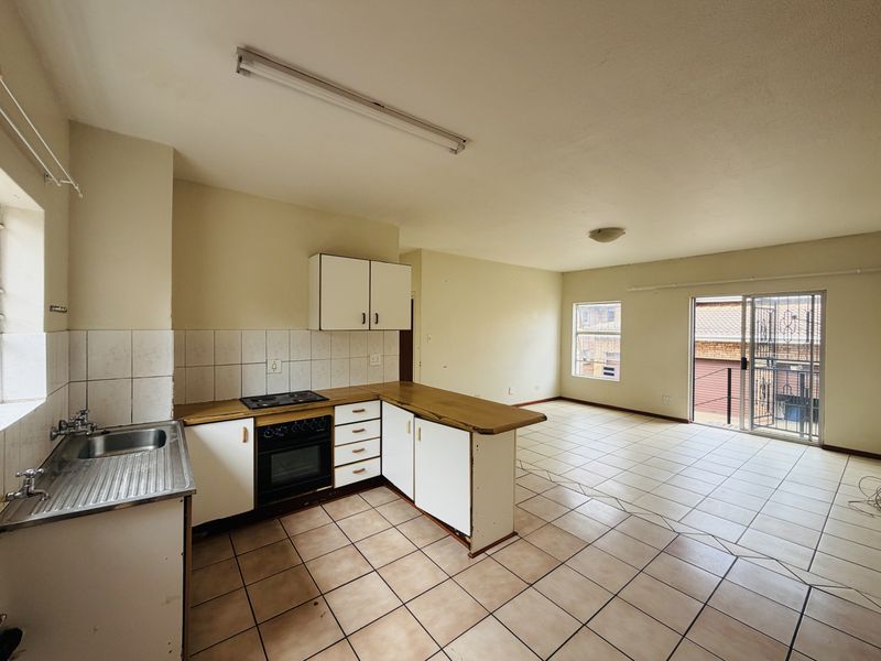 Open-plan kitchen and living area featuring tiled flooring, built-in cabinetry with an integrated oven and hob, and access to a balcony via sliding doors.