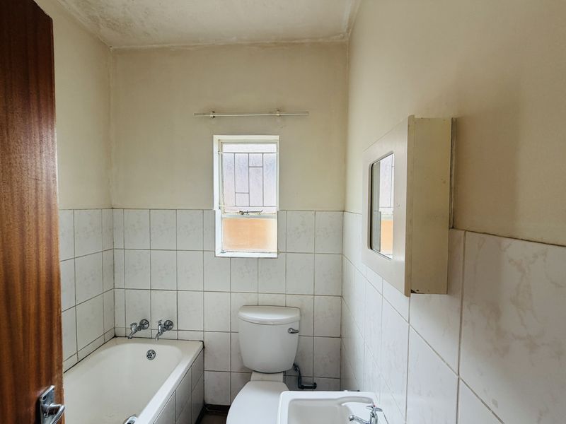 A dated bathroom featuring a bathtub, toilet, and wall-mounted basin with tiled walls and a medicine cabinet.