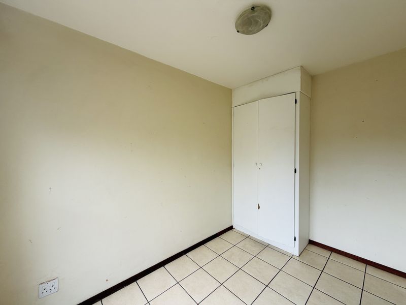 An empty bedroom featuring tiled flooring and a built-in cupboard, offering a blank canvas for potential renovation or interior design updates.