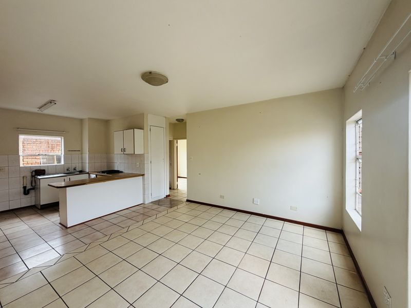 Open plan living and kitchen area featuring tiled flooring, built-in cabinetry, and a breakfast counter in a neutral, vacant space.