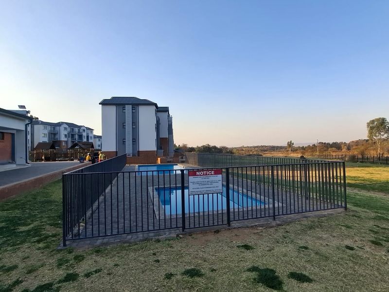 A communal swimming pool area featuring a paved surround and metal safety fencing, situated within an apartment complex grounds.