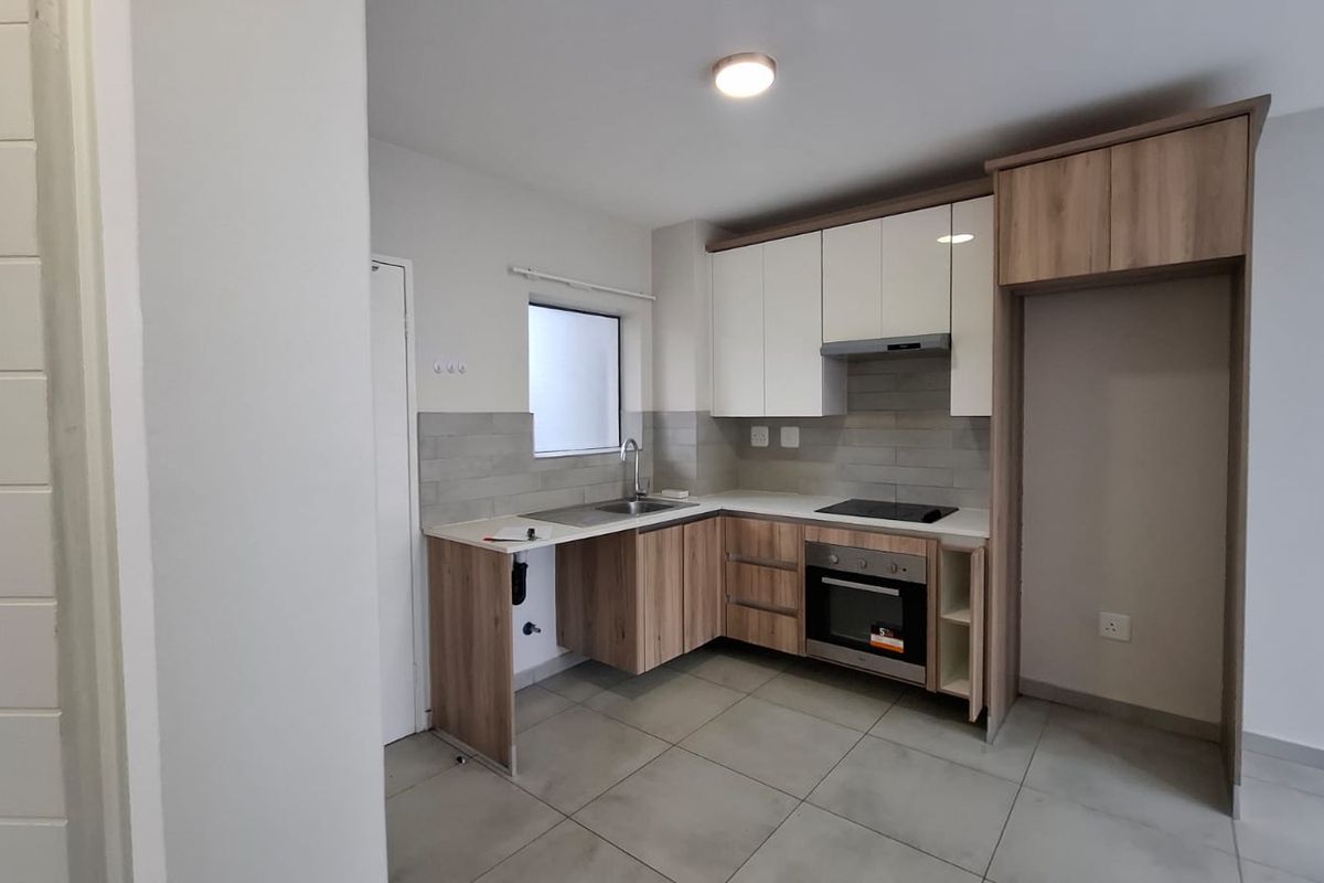 Modern kitchen featuring sleek two-tone cabinetry, integrated electric hob and oven, stainless steel sink, and neutral tiled flooring.