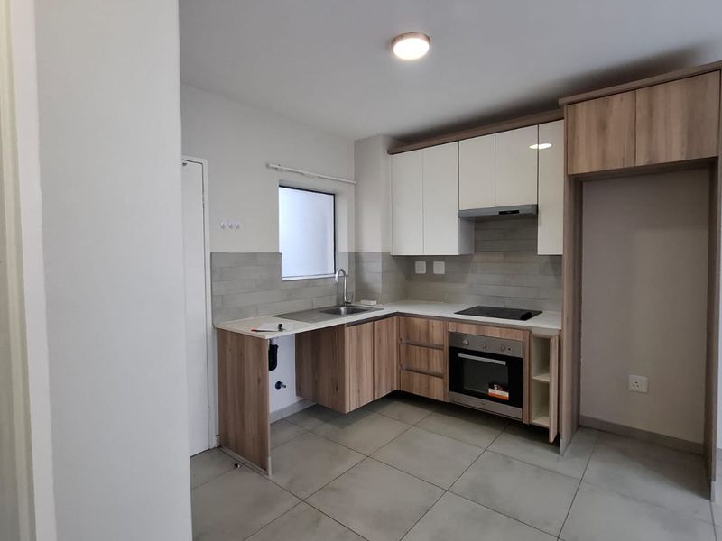 Modern kitchen featuring sleek two-tone cabinetry, integrated electric hob and oven, stainless steel sink, and neutral tiled flooring.