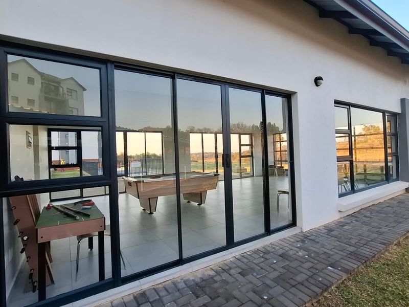 Rear exterior view of the apartment featuring large sliding glass doors, a paved walkway, and a well-maintained tiled patio area.
