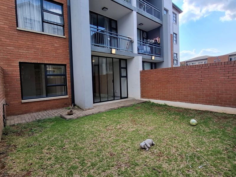 A private rear garden featuring a paved patio area, enclosed by brick boundary walls, with direct access to the apartment via sliding glass doors.