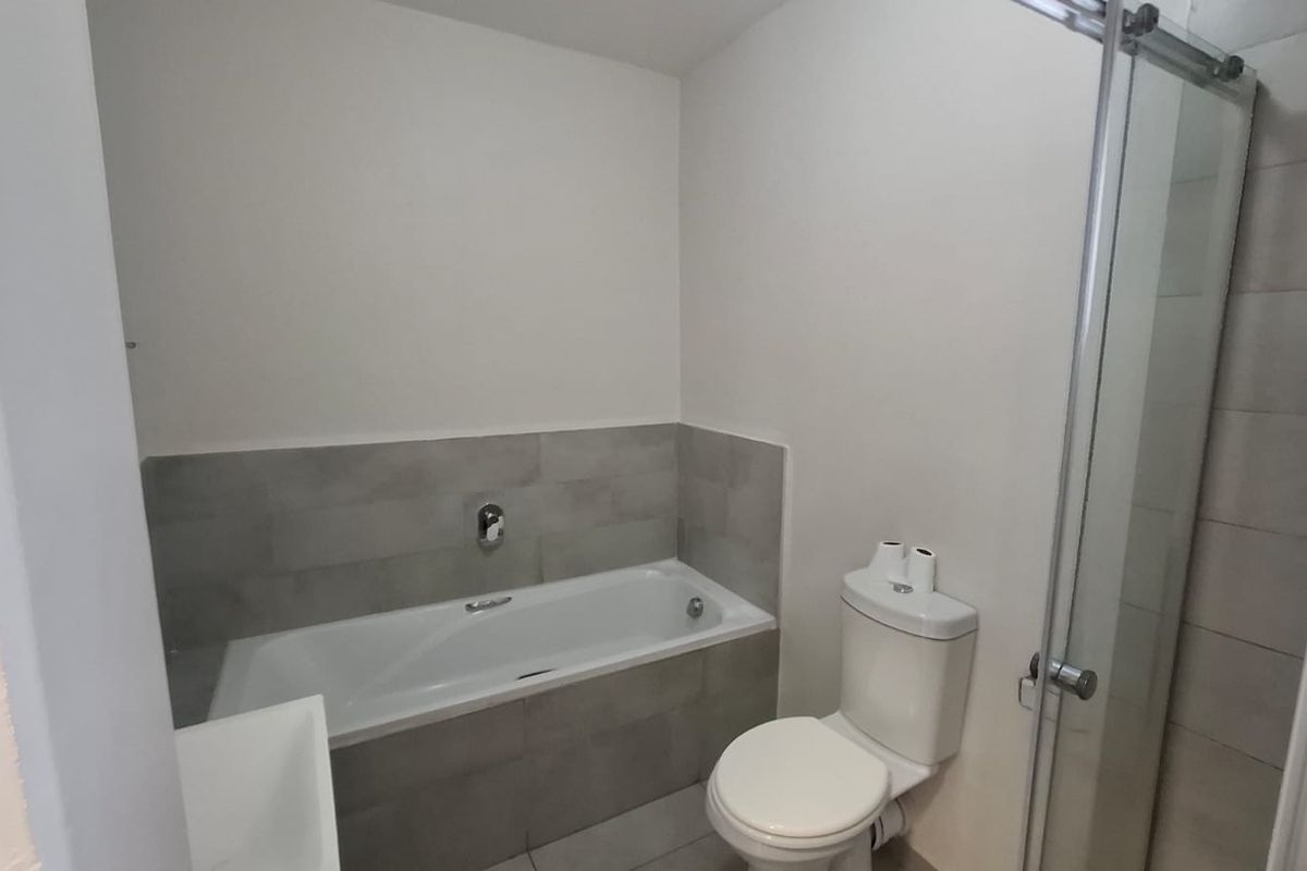 A clean, modern bathroom featuring a bathtub, a separate shower enclosure with glass door, and neutral grey tiling.