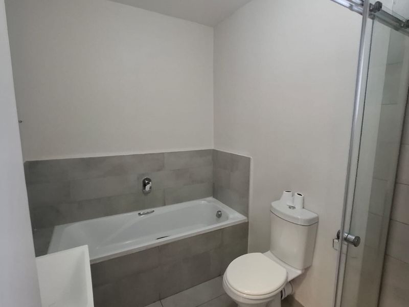 A clean, modern bathroom featuring a bathtub, a separate shower enclosure with glass door, and neutral grey tiling.