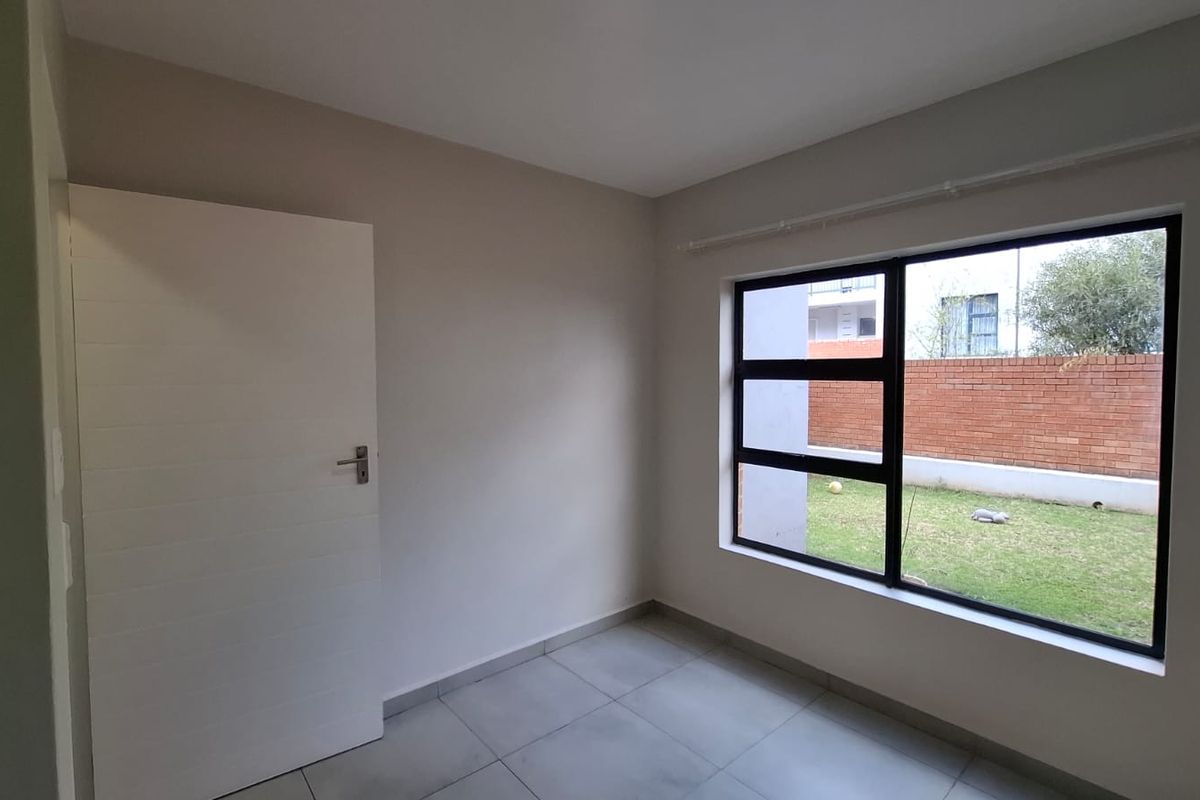 A bright, empty bedroom featuring neutral walls, tiled flooring, and a large window overlooking the garden area.