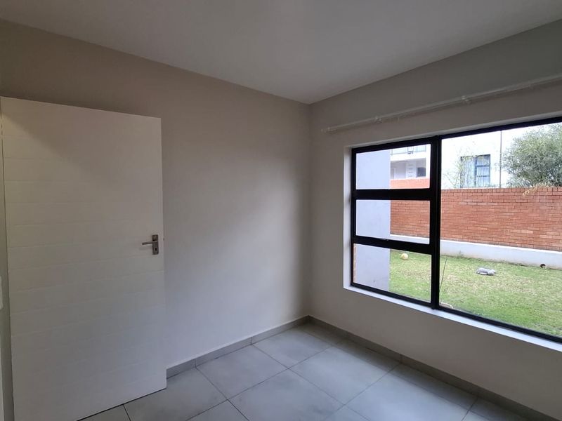 A bright, empty bedroom featuring neutral walls, tiled flooring, and a large window overlooking the garden area.