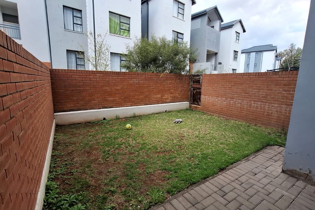 A private rear garden featuring a paved patio area, a small lawn, and enclosed by brick boundary walls.