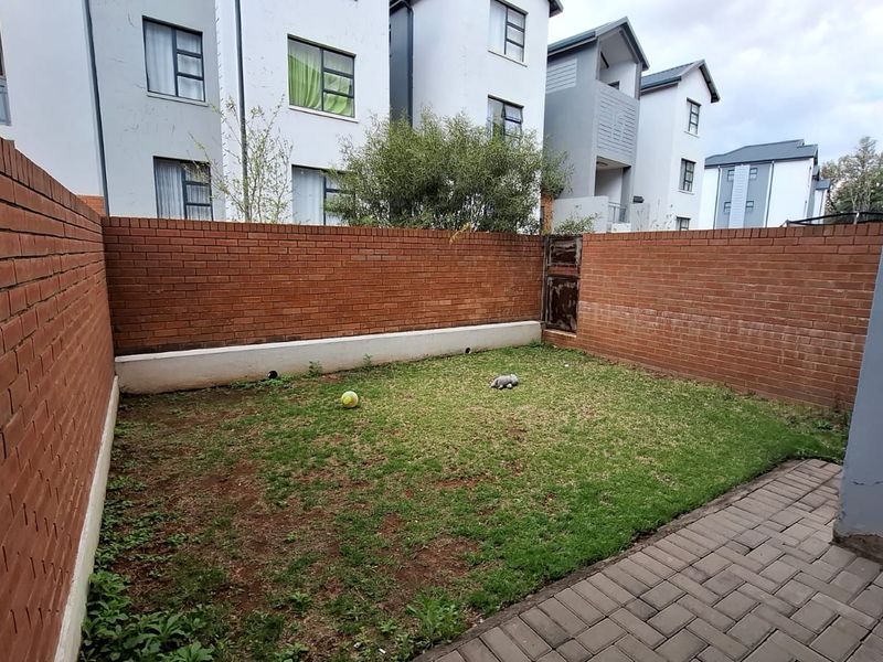 A private rear garden featuring a paved patio area, a small lawn, and enclosed by brick boundary walls.