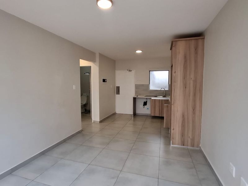 An open-plan living and kitchen area featuring neutral tiled flooring, modern cabinetry, and recessed lighting, leading to an adjacent bathroom.