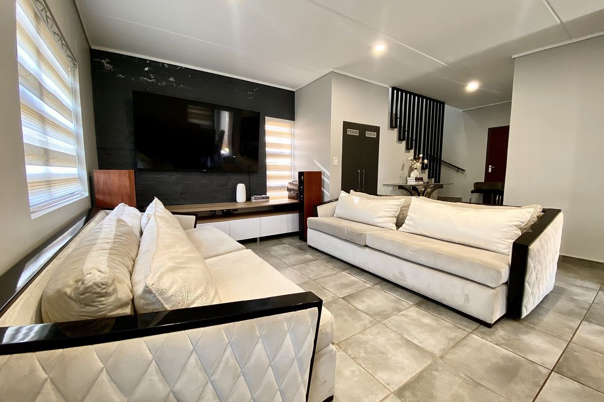 Modern living room featuring large format floor tiles, recessed lighting, a feature wall, and a staircase with contemporary vertical balustrades.