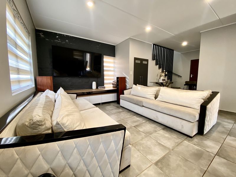 Modern living room featuring large format floor tiles, recessed lighting, a feature wall, and a staircase with contemporary vertical balustrades.