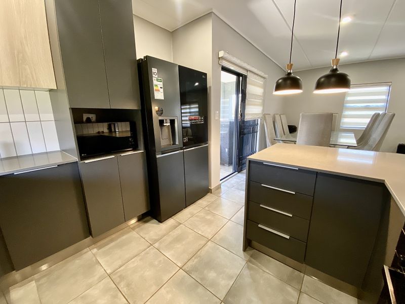 Modern open-plan kitchen and dining area featuring sleek dark cabinetry, stone countertops, tiled flooring, and direct access to an outdoor patio space.