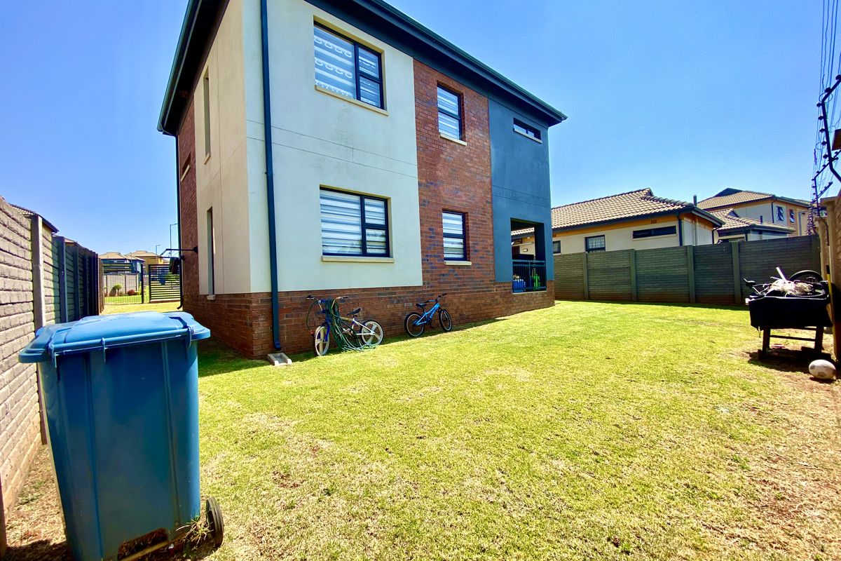 A view of the rear elevation of a modern double-storey house featuring a combination of brick and plastered finishes with a private garden area.