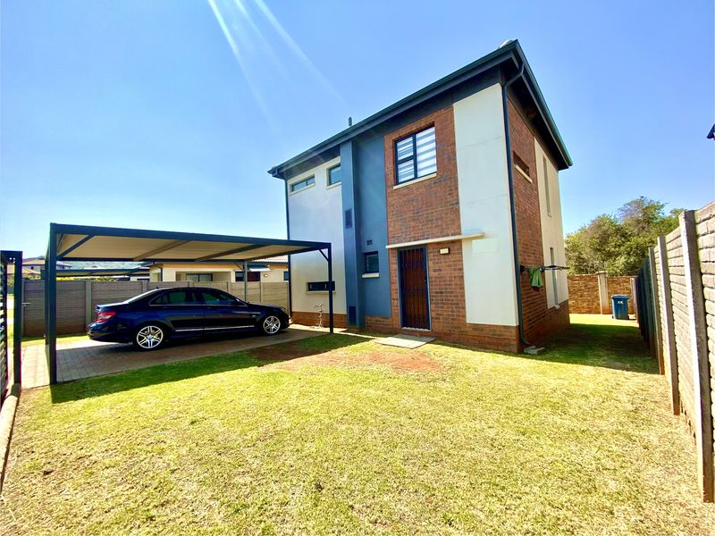 Rear view of a modern two-story brick and plaster house featuring a covered carport, paved driveway, and a private garden area.
