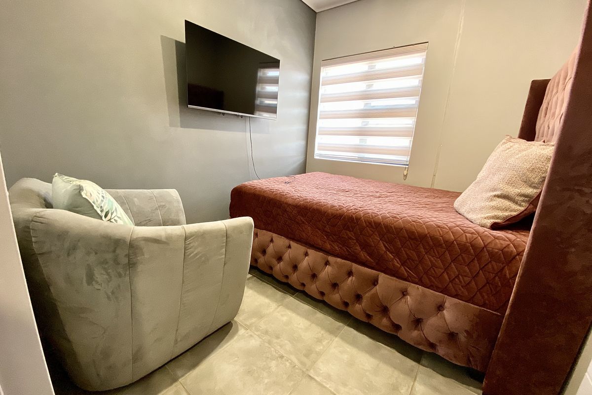 A compact bedroom featuring tiled flooring, neutral wall finishes, and a wall-mounted television, providing a functional and modern living space.