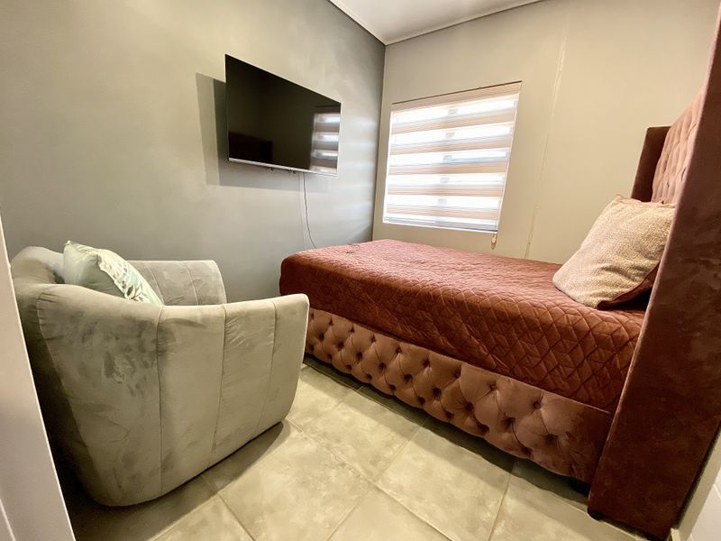 A compact bedroom featuring tiled flooring, neutral wall finishes, and a wall-mounted television, providing a functional and modern living space.