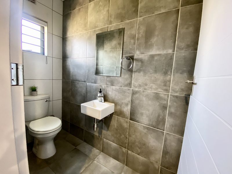 A modern, compact guest bathroom featuring floor-to-ceiling tiled walls, a wall-mounted basin with chrome fixtures, and a standard toilet.