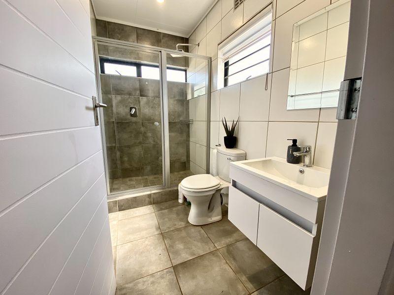 A modern, well-maintained bathroom featuring a glass-enclosed shower, a contemporary vanity with basin, and neutral floor-to-ceiling tiling.