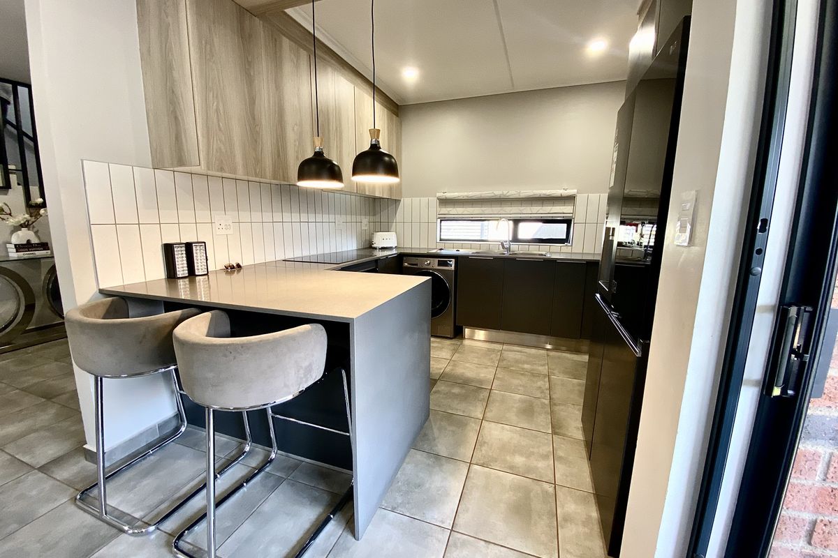 Modern kitchen featuring sleek cabinetry, stone countertops, a breakfast bar, tiled backsplash, and integrated appliances in a contemporary open-plan layout.